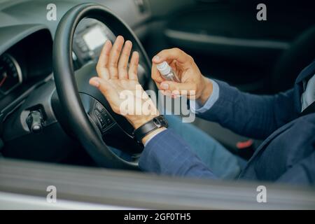 Businessman using disinfectant spray while sitting in car Stock Photo