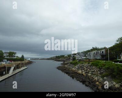 A view of a small town or a village on a cloudy day. River along rocky water edge with houses around Stock Photo