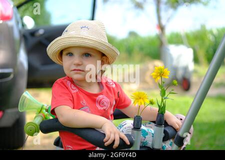 Close-up of a cute little girl in a hat. Portrait of a lovely little girl in a summer hat looking at the camera sitting on a bicycle. Stock Photo