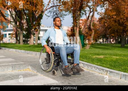 Paraplegic black guy in wheelchair going down ramp on on walk at park in autumn, using impaired friendly facilities