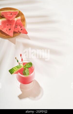 Glasses of watermelon Margarita cocktail with mint and ice. Summer refreshing drinks in glasses with shadows from tropical leaves on a white backgroun Stock Photo