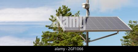 Solar powered surveillance camera. Solar panels powering a surveillance camera in a city park against a background of blue sky. Safety and clean Stock Photo