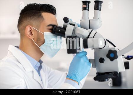 Arab Male Medical Worker Using Microscope, Making Research In Modern Laboratory Stock Photo