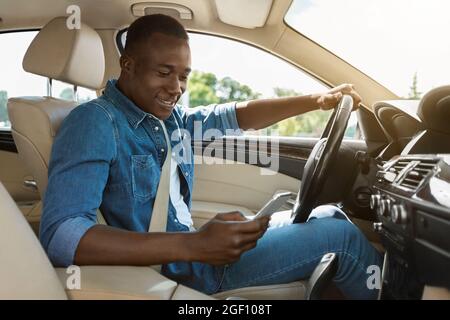 Smiling black guy using smartphone while driving car Stock Photo