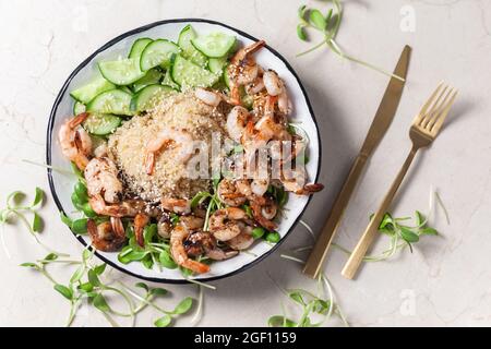 Quinoa with grilled prawns or shrimps, cucumber and micro greens on the marble background. Stock Photo