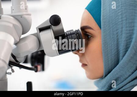 Side View Of Islamic Female Dentist Doctor In Hijab Using Dental Microscope Stock Photo