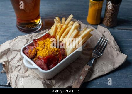 Currywurst with french fries in white bowl on craft paper served with beer. Stock Photo