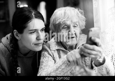 An granny old woman looks at a smartphone, with his adult granddaughter. Black and white photo. Stock Photo