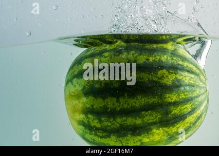 Close up view of  watermelon falling in water on turquoise background.  Gorgeous backgrounds. Stock Photo