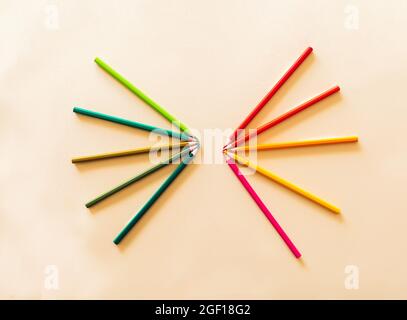 composition of colored pencils in shades of red, yellow and green, placed in fans facing each other on a yellow background with a back to school conce Stock Photo