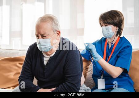 Medical nurse doing checkup to senior man patient during coronavirus outbreak home visit - Focus on man face Stock Photo