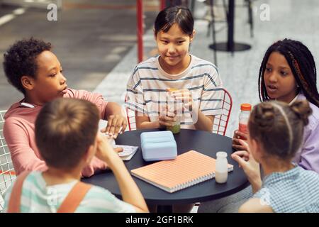Portrait of multi-ethnic group of children sitting at table outdoors during lunch at modern school Stock Photo