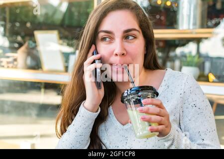 A young Israeli woman sipping her drink at a cafe while talking with her friends on the phone Stock Photo