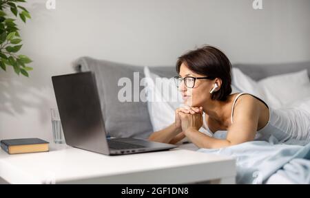 Woman lying on bed with laptop Stock Photo