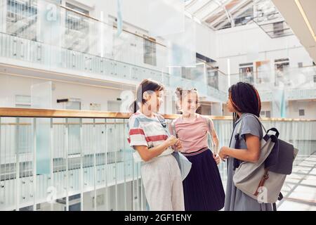 Portrait of three schoolgirls chatting in school while standing in sunlight under glass ceiling, copy space Stock Photo