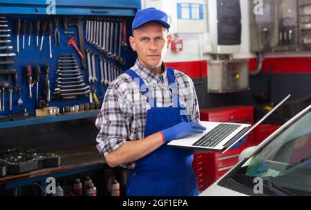 Mechanic man using laptop checking car in workshop Stock Photo