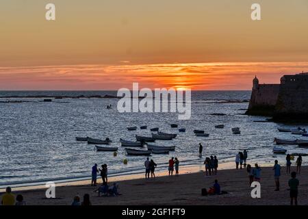 Backlit image of a beach in Cadiz (Spain) at sunset, showing people and boats moored after fishing, on a beautiful summer day. Stock Photo