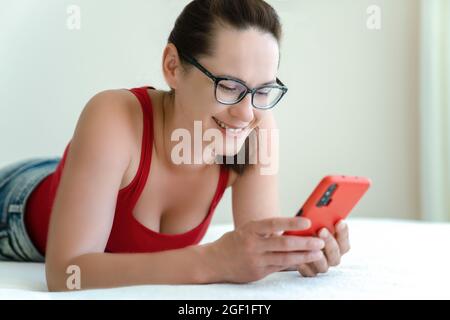 Woman talk via a smartphone video camera with positive emotions on her face while lying on bed. Stock Photo