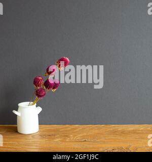 Vase of purple globe amaranth flowers on wooden table. gray wall background. copy space Stock Photo
