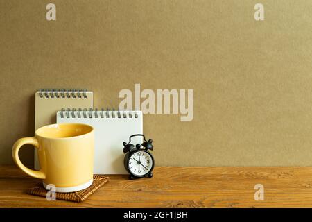 Notebook, mug cup, clock on wooden desk. brown wall background. workspace Stock Photo