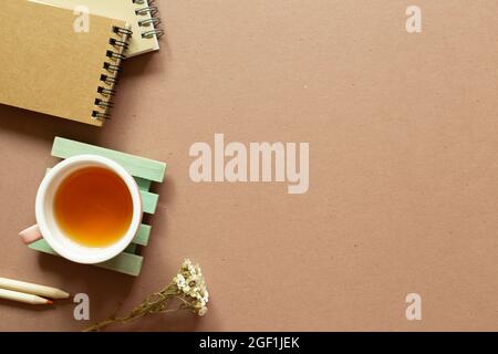 Notebook, colored pencil, dry flower, tea cup on brown background. flat lay, top view, copy space. Work and study place Stock Photo