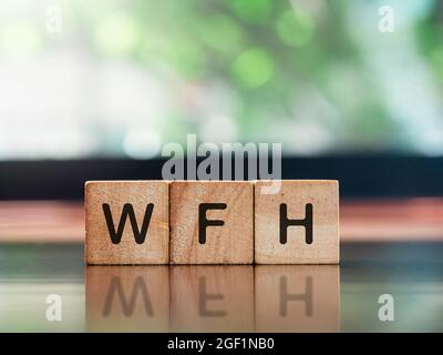 Work from home concept. WFH, words on wooden cube blocks on brown wood desk and green nature background with copy space. Stock Photo