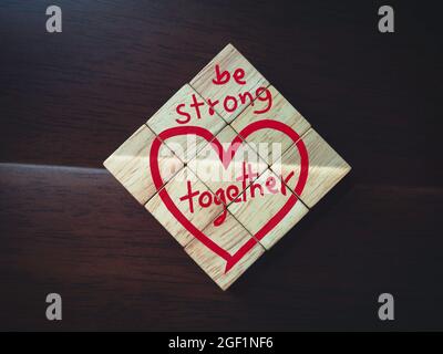 Be strong and together, words and red heart on wooden cube blocks on dark brown wood background. Stock Photo
