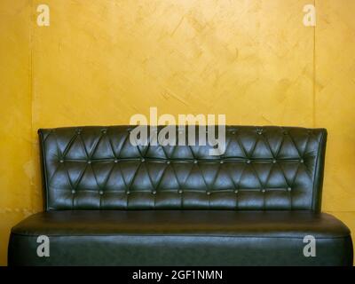 Dark green vintage leather sofa seat with pins and buttons on yellow wall background in the living room with copy space. Stock Photo