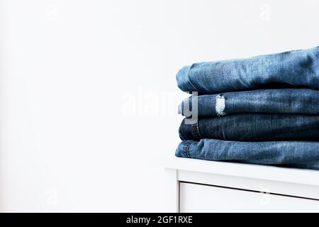 Stack Of Different Jeans On Table Against White Background. Space For 