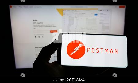 Person holding smartphone with logo of US collaboration platform company Postman Inc. on screen in front of website. Focus on phone display. Stock Photo