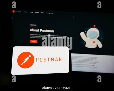 Person holding mobile phone with logo of US collaboration platform company Postman Inc. on screen in front of web page. Focus on phone display. Stock Photo