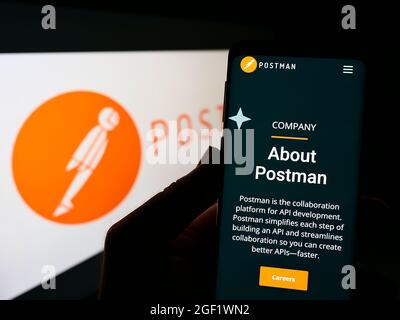 Person holding cellphone with website of US collaboration platform company Postman Inc. on screen with logo. Focus on center of phone display. Stock Photo