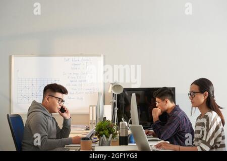 Young IT specialists working on computers in modern office with big whiteboard Stock Photo