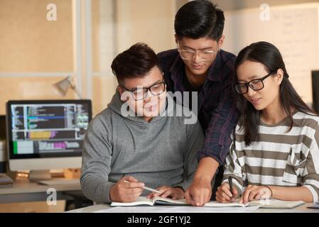 Smart positive college student helping friends with doing project for computer science class Stock Photo