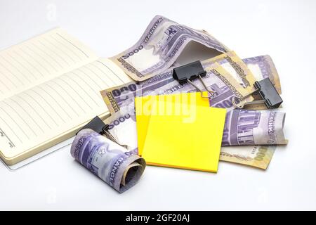 Scattered thousand taka bangladesh banknotes with a notebook, black binder, and sticky notes on white background Stock Photo
