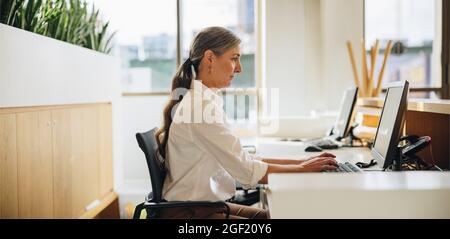 Side view of woman working on computer at desk in office. Female executive using computer at work Stock Photo