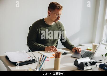 Man sitting at his office desk busy working on laptop. Male entrepreneur working on a project alone. Stock Photo