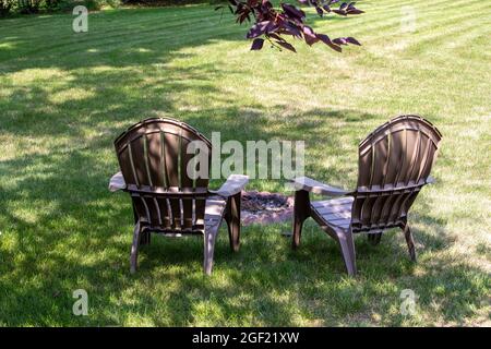 Close up backside view of a pair of gray lawn chairs facing a fire pit, in a back yard with light shade Stock Photo