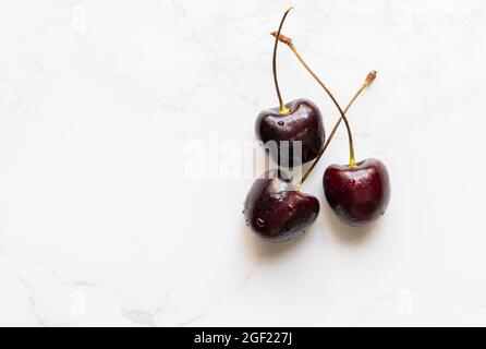 Top view fresh red cherries on marble floor, flat lay design, group of three fresh red cherries, small water drop on the fruit. Stock Photo