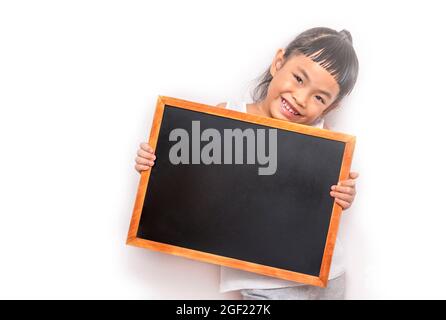 Asian child girl holding the small blank blackboard or chalkboard. Back to school concept. Child wearing white cloth. Looking at the camera. Big smile Stock Photo