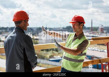 Portrait of two construction workers discussing project while standing at high rise building Stock Photo