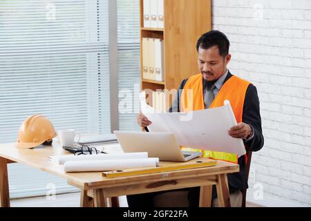 Head contractor working with documents, he is rolling out construction plan Stock Photo