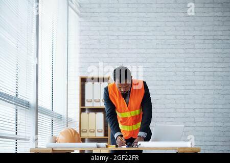 Construction engineer in orange west over suit making final corrections in building blueprint Stock Photo