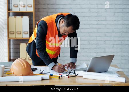 Civil engineer in range vest making corrections in construction plan on his office table Stock Photo