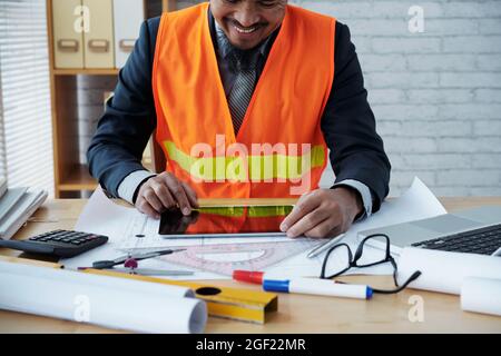 Positive construction engineer zooming in blueprint on tablet computer to checking every detail Stock Photo