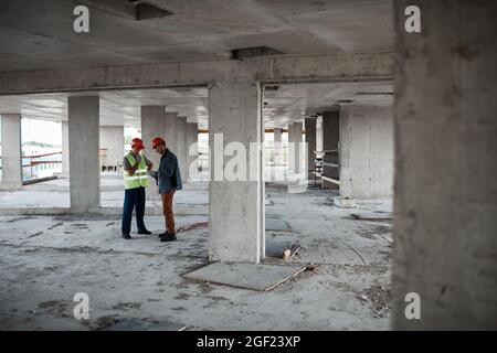 Wide angle view at two building contractors discussing project while standing at construction site, copy space Stock Photo
