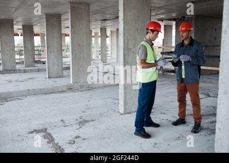 Full length portrait of two building contractors discussing project while standing at construction site, copy space Stock Photo