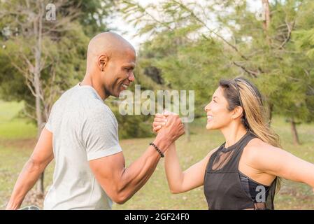 Close up of an ahlete couple exercising by holding with one hand in the park Stock Photo
