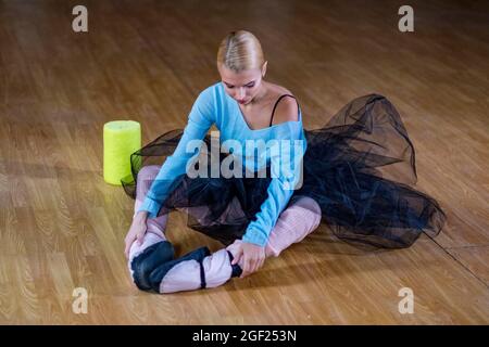 Female ballet dancer performs stretching exercises before beginning a dance rehearsal. Stock Photo