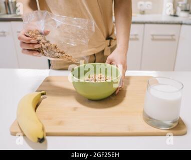 Young woman pours granola into a plate for breakfast. Stock Photo